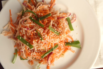 Vegan salad with carrot and radish. Asian cuisine. Healthy vegetarian appetizer on the round plate. Side dish. Simple low calories lunch. Top view.