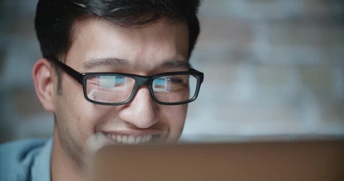 young positive asian student smiles while working at computer in loft room 4k dollyshot