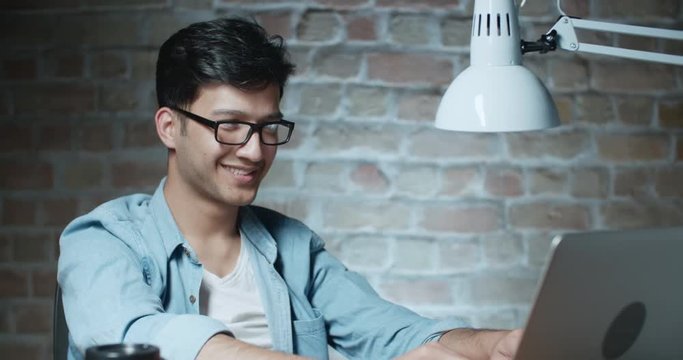 young positive asian student smiles while working at computer in loft room 4k dollyshot