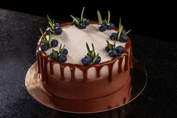 Chocolate cake with blueberries on a black background, decorated with small green leaves and fresh berries