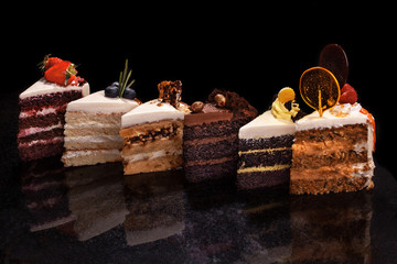 Izabrani veliki komadi različitih kolača: čokolada, maline, jagode, orašasti plodovi, borovnice. Komadi kolača na crnom stolu.