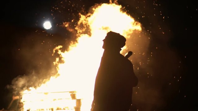 Revolution destructive behavior guy on the car with a baseball bat breaks glass. In the background is a fire. shooting at night