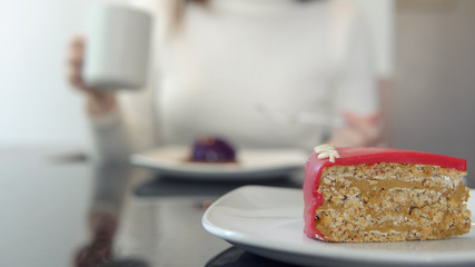Close-up of delicious dessert in focus. young girl drinks coffee and eats cake in blurred background