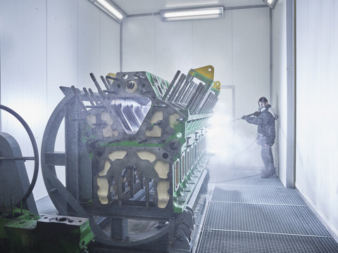 Worker cleaning engine block in washing bay
