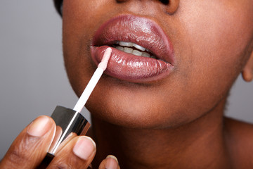 Close up beautiful african american woman applying shiny lip gloss - obrazy, fototapety, plakaty