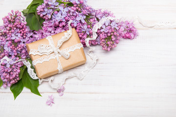 Lilac flowers and gift box on white wooden background, copy space