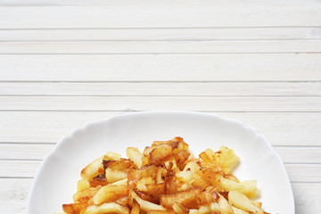 Fried potatoes in a white plate on a white wooden background.