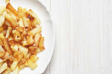 Fried potatoes in a white plate on a white wooden background.