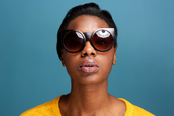 stylish young black woman in sunglasses by blue wall
