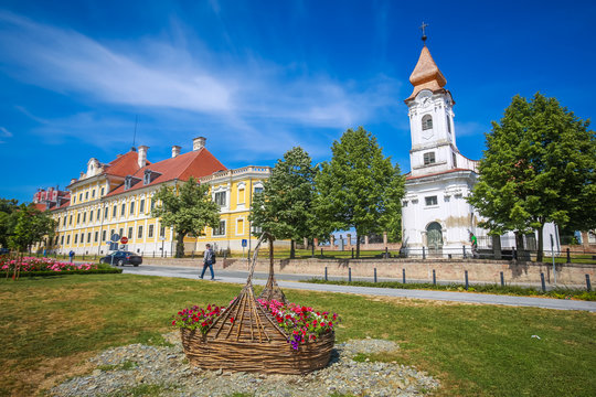 View of a large straw basket with flowers in a park with people walking in the street and the City museum and Chapel of the Saint Roko in the background in Vukovar, Croatia.