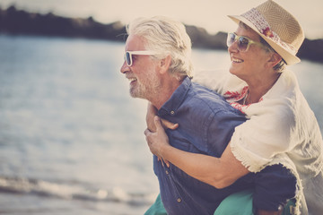 happy senior couple have fun and enjoy outdoor leisure activity at the beach. the man carry the...