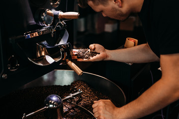 Man working at coffee production. Barista controling coffee grounds roasting process. - obrazy, fototapety, plakaty