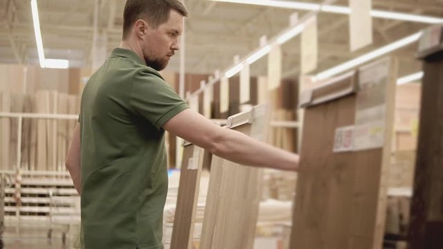 Side view shot of a man looking at and choosing parquet in a building store. Man is taking demonstration sample of parquet and looking it over.