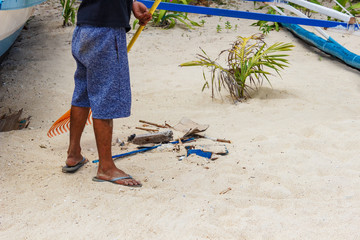 An employee is cleaning the beach. Rake for a tool to get hay from the sea and garbage disposal from the beach. White sandy beach.