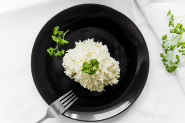 Cabbage salad with a sprig of parsley on a black plate on a white table, top view