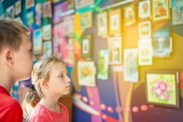 The boy and girl at the exhibition of paintings and photographs attentively looks at the painting and enjoys the art.