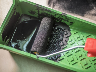 close up hand put roller tool in black colour paint in green tray in workshop