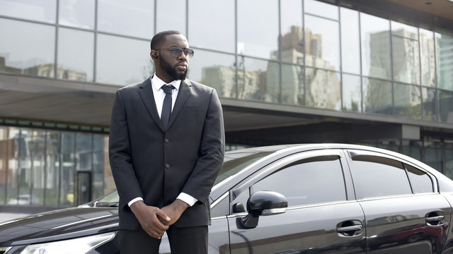 Confident Afro-American driver standing by car, security guard service, business