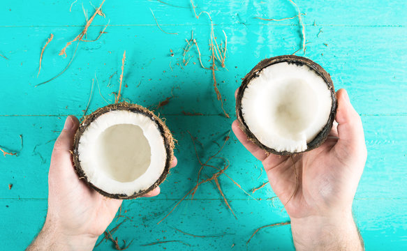 Two halves of chopped coconut in hands on a blue background with peel