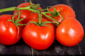 Branch of ripe tomatoes on black wooden background