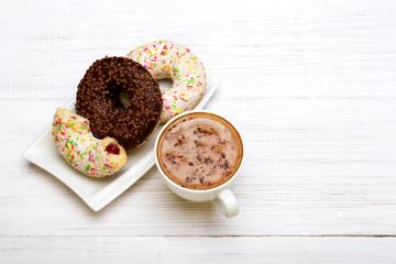 Cup of coffee and tasty donuts with icing and chocolate on white wooden background, copy space