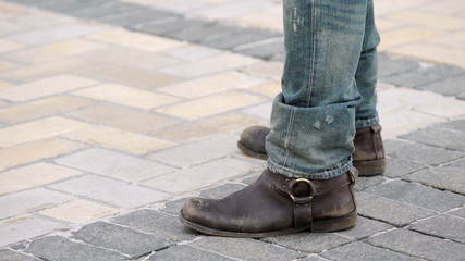 Man with brown boots and ripped jeans standing next to motorcycle, tough biker