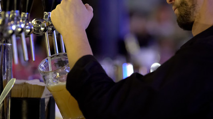 Barman professionally fills up glass of unfiltered wheat beer, pouring technique