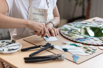 Workplace of the mosaic master: women's hands holding tool for mosaic details in the process of...