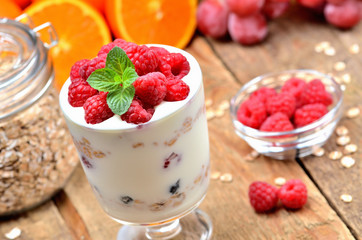 Homemade bio yogurt, raspberries and mint leaves, oranges, grapes and glass of oatmeals in background - healthy breakfast concept