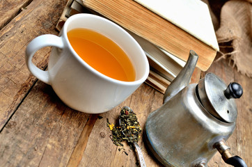 Close-up of stack of old, vintage books, mug of black tea, old teapot and spoon with tea loose