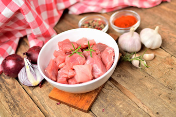Pork raw meal diced in a bowl, garlic, half of onion, colored and sweet pepper, checkered red tablecloth in the background