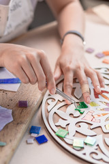 Workplace of the mosaic master: women's hands holding tool for mosaic details in the process of making a mosaic
