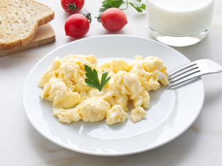white plate with pan-fried scrambled eggs on a white light background with tomatoes. Omelette, side view