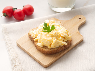 Sandwich with pan-fried scrambled eggs on wooden cutting board, side view.