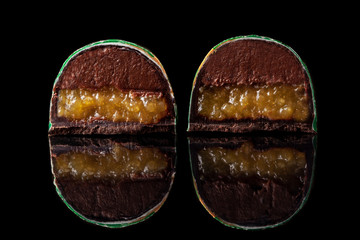 Cut luxury handmade candy with chocolate and yellow confiture filling on black background.
