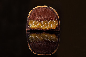 Cut luxury handmade candy with chocolate and yellow confiture filling on black background.