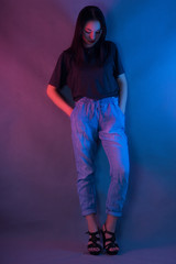A young girl in blue jeans and a black t-shirt stands on a blue-pink background