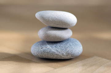 Obraz na płótnie Canvas Group of zen stones pile, grey meditation pebbles tower on light brown wooden background in sunlight