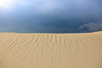 Fale na piaseku na tle pochmurnego nieba, i w promieniach zachodzącego słońca, wydma, pustynia.