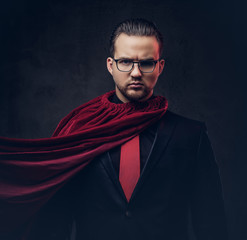 Portrait of a genius superhero in a black suit with a red tie on a dark background. 