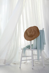 Fototapeta na wymiar Sun hat on a white chair with a blue sarong next to an open window and a summer breeze