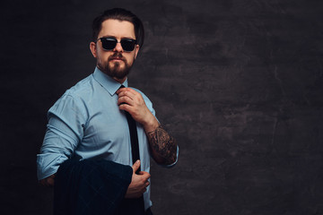 Portrait of a handsome middle-aged man with beard and hairstyle dressed in formal clothes sunglasses, straightens the tie and holds a jacket.