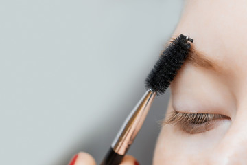 Young woman combs her eyebrows with brush in beauty salon, concept of hair correction.