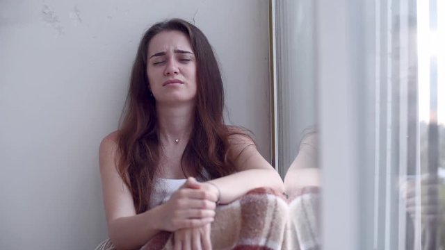 Young depressed woman is beats her head against the wall sitting on the floor by the window with rain falling outside. Lonely woman suffering emotional distress or violence with the suicide thoughts
