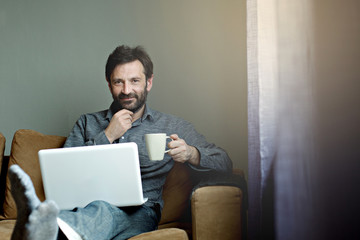 Man working on laptop, drinking coffee and smile. Home interior, businessman, domestic life 