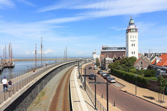 View on the white Harlingen lighthouse in The Netherlands with railroad, sea and sailing ships against a blue sky