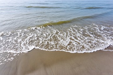 Blue green waves reaching sandy beach in the Netherlands   
