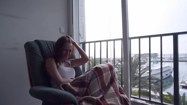 Young depressed woman suffering a distress and crying sitting in chair by the window with the sea view. Raining outside. Lonely woman in despair.