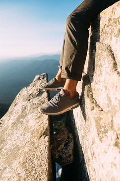 Man In Tennis Shoes Hanging Legs Over Edge of Rock