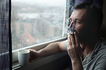 Man with morning coffee cup smoking cigarette by the window